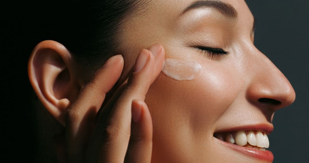 Mulher caucasiana sorri ao aplicar seu creme de hidratação facial em seu rosto